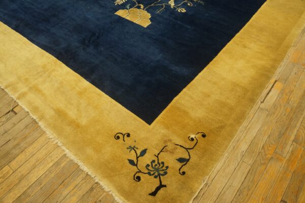 A deep blue rug field with gold floral patterns meets a wide golden border on worn wood planks.