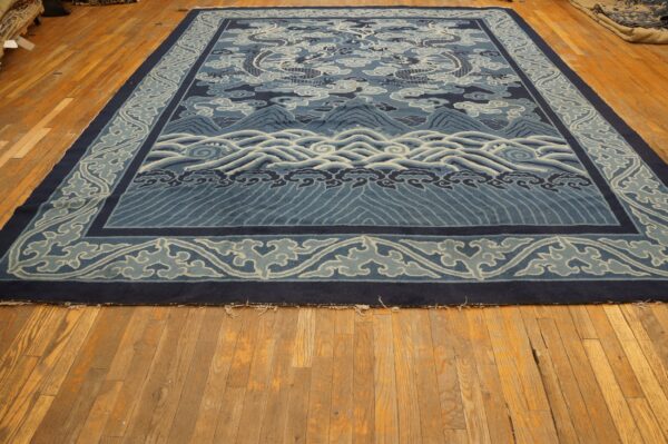 A large blue rug featuring dragons, clouds, mountains, and waves rests on rustic hardwood flooring.