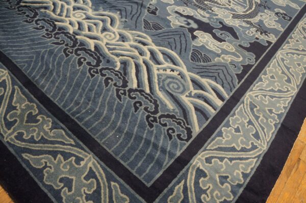 Blue low-pile rug with ornate waves, clouds, and border designs resting on wood flooring.