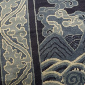 Dark blue rug with stylized light blue borders, mountains, and waves on a wooden floor.