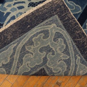 Dark blue ornate rug with scroll patterns is folded over, exposing its woven foundation on wood planks.