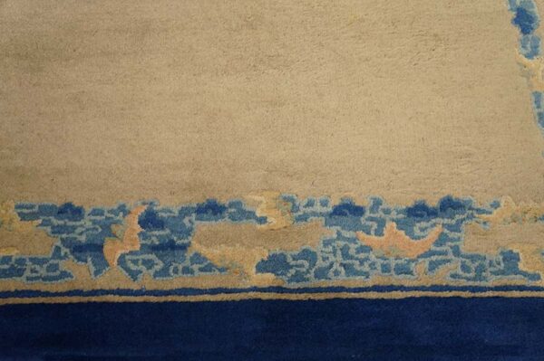 A beige rug field transitions to a decorative border featuring blue cloud shapes and a solid dark blue band.