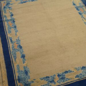 Tan rug with a wide navy blue border and abstract light blue and orange patterns, resting on wood planks.