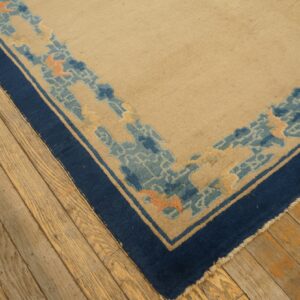 Beige rug corner featuring a navy blue edge and abstract border pattern in blue and peach on wooden planks.