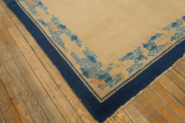 Beige rug corner featuring a navy blue edge and abstract border pattern in blue and peach on wooden planks.