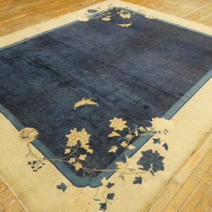 A cream-bordered blue rug with stylized floral patterns and a moth motif lies on light wooden flooring.