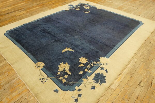 A cream-bordered blue rug with stylized floral patterns and a moth motif lies on light wooden flooring.