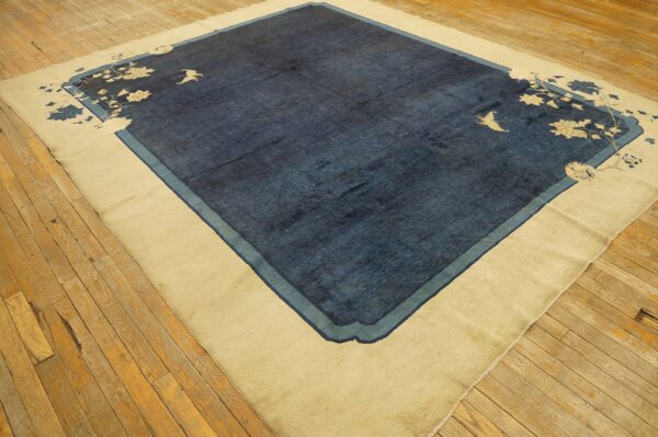 Dark blue rug featuring a wide beige border and subtle corner floral and bird designs on wood floors.