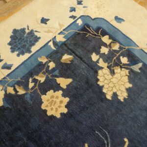 Detail of a navy and cream floral rug border folded on distressed light wood flooring.