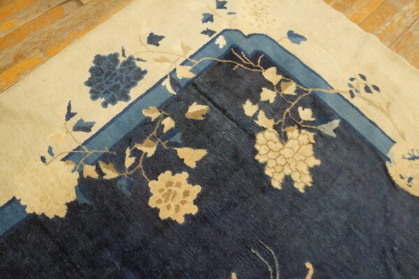 Detail of a navy and cream floral rug border folded on distressed light wood flooring.