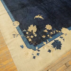 Dark blue rug featuring cream and light blue florals along a wide cream border on wood flooring.