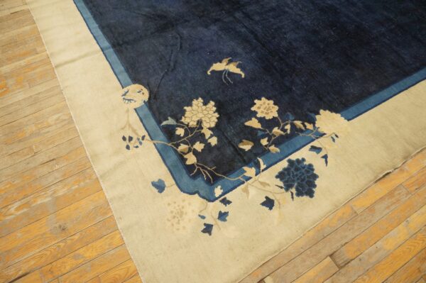 Dark blue rug featuring cream and light blue florals along a wide cream border on wood flooring.