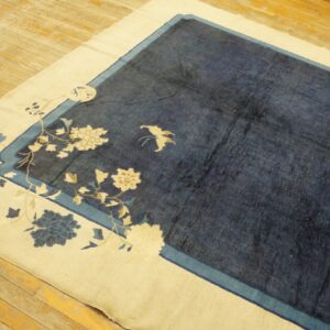 A navy rug with a cream border featuring floral patterns lies on worn wooden floorboards.