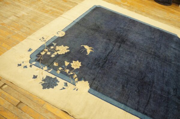 A navy rug with a cream border featuring floral patterns lies on worn wooden floorboards.