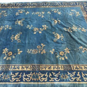 Blue rug with light tan scattered floral sprigs and multiple borders displaying geometric patterns.