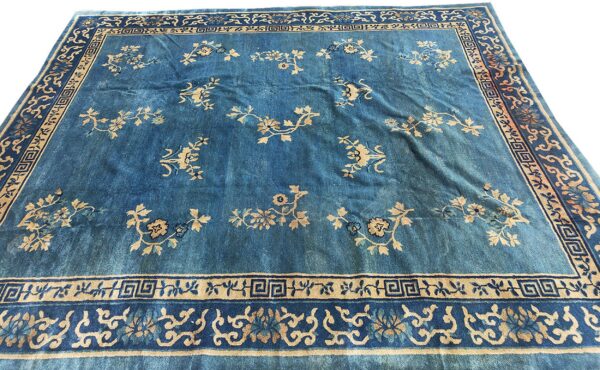 Blue rug with light tan scattered floral sprigs and multiple borders displaying geometric patterns.