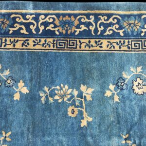 Detailed view of a blue and beige floral rug with multiple border bands including a Greek key design.