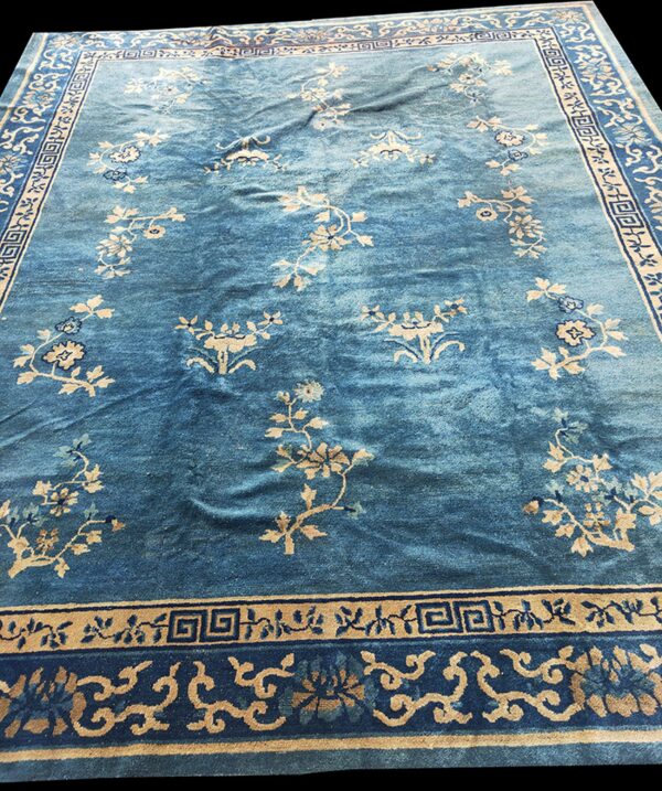 Low-pile blue rug with scattered tan floral motifs and complex multiple geometric borders.