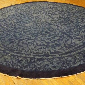 Circular dark blue rug with faded traditional scrolling and dragon motifs lying on wood planks.