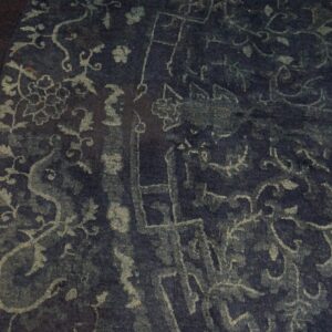 Dark navy rug with faded light blue traditional patterns rests on a brightly lit yellow hardwood floor.