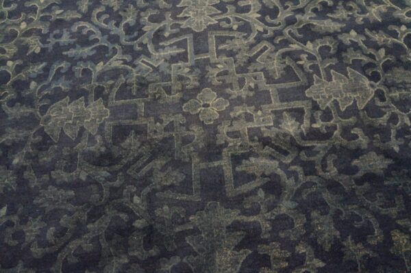 Dark blue rug with a muted teal and grey traditional pattern of intertwining florals and angular motifs.