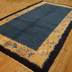 Indigo and gold rug featuring a subtle fretwork field and a wide floral-and-object border on wood flooring.