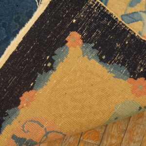 Blue, beige, and coral high-pile rug folded over to show the woven backing on rustic wood flooring.