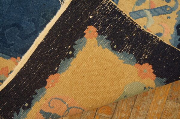 Blue, beige, and coral high-pile rug folded over to show the woven backing on rustic wood flooring.