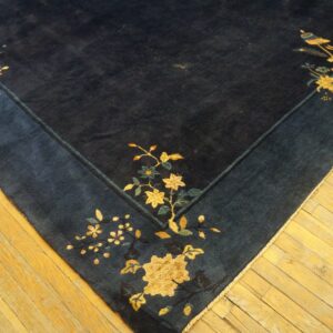 A navy blue rug with gold and teal floral and vase motifs lies on light yellow hardwood floors.