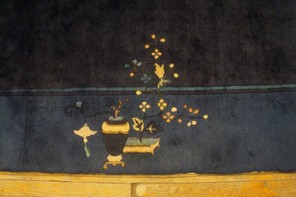 Navy rug detail showing a stylized yellow vase and floral design over exposed wood flooring.