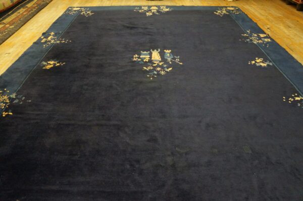 A deep navy blue rug features stylized floral and figural motifs, displayed on light wood floors.