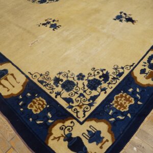 Cream rug with indigo blue and brown floral border and field accents resting on worn wood planks.