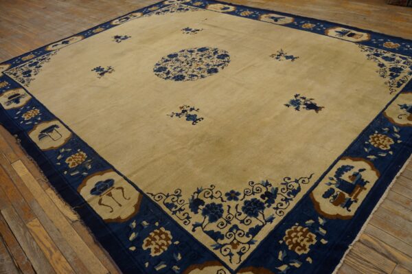 Beige square rug with an elaborate navy blue border and scattered designs on wood flooring.