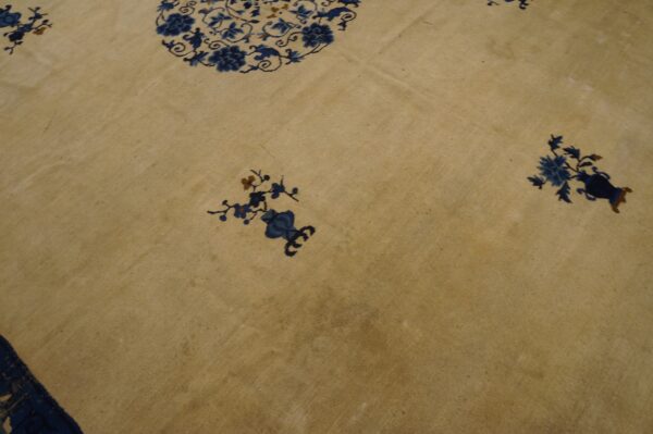 Tan area rug featuring scattered dark blue floral vases and a partial medallion motif.