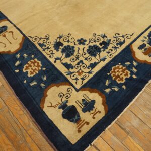 Corner detail of a tan rug with dark blue border and stylized blue and brown floral patterns on wood floors.
