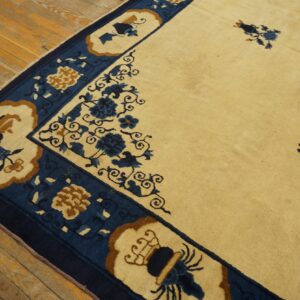 Cream rug featuring a wide dark blue border with tan and blue floral motifs on distressed wood flooring.