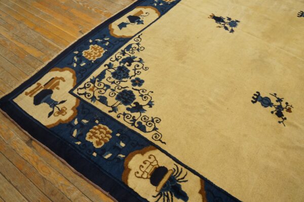 Cream rug featuring a wide dark blue border with tan and blue floral motifs on distressed wood flooring.