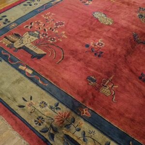 Muted red high-pile rug with blue, beige, and green floral patterns rests on light hardwood flooring.