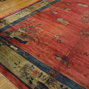 Deep pink rug with scattered motifs and a contrasting olive green and blue floral border on wood flooring.