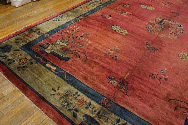 Deep pink rug with scattered motifs and a contrasting olive green and blue floral border on wood flooring.