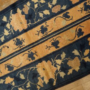 Navy blue runner rug featuring large tan floral designs and horizontal ochre pattern bands on wood.