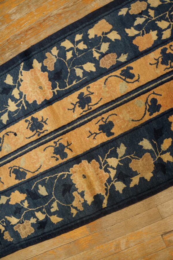 Navy blue runner rug featuring large tan floral designs and horizontal ochre pattern bands on wood.