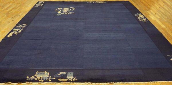 Deep navy rug with light pictorial corner and center motifs displayed on light wood floorboards.