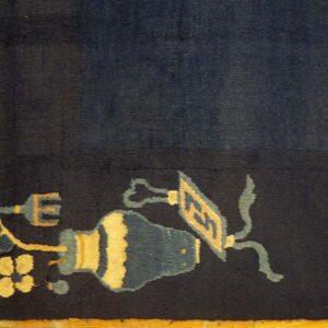 Deep navy rug edge features a border of stylized yellow and teal floral and vessel motifs on wood flooring.