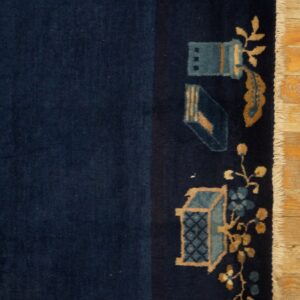 Close view of a dark blue rug showing stylized teal and tan motifs and white fringe on a wood floor.