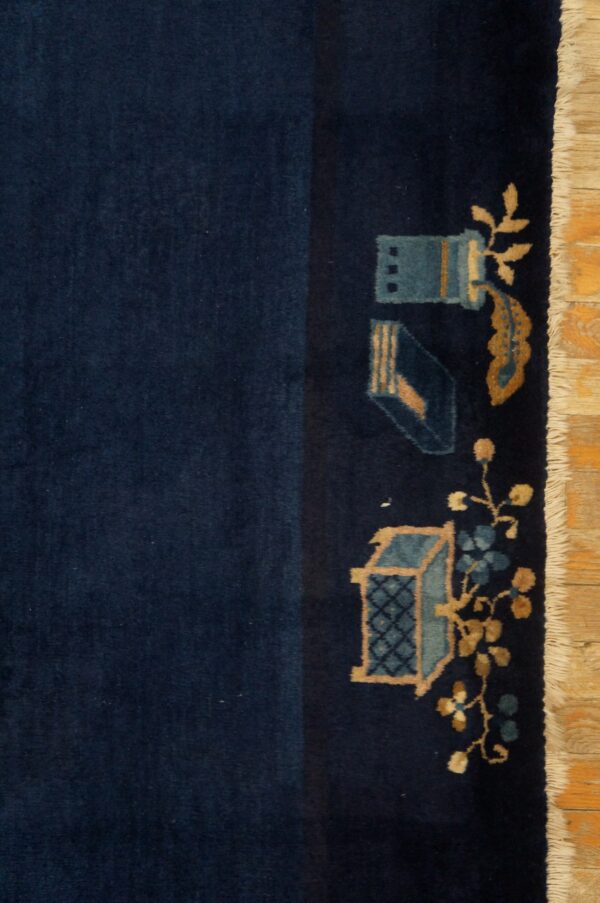 Close view of a dark blue rug showing stylized teal and tan motifs and white fringe on a wood floor.