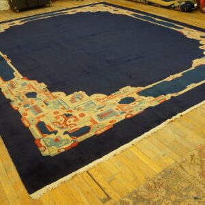 Large navy blue rug with a geometric border in cream, light blue, and coral on an aged wood floor.