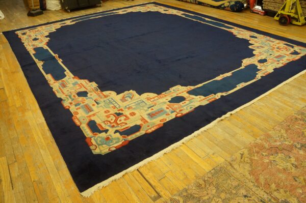Large navy blue rug with a geometric border in cream, light blue, and coral on an aged wood floor.
