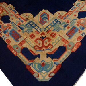 Close-up detail of a high-pile rug featuring a navy blue field and a complex geometric border in tan, red, and blue.