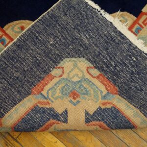 The rug is folded to show its tightly woven navy backing above the colorful low-pile geometric pattern on wood.